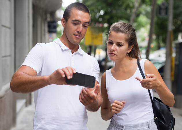  Ein Mann und eine Frau stehen auf einer Straße und schauen gemeinsam in ein Handy.