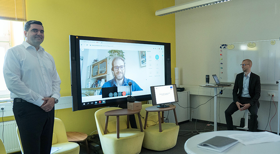 Zwei Männer stehen vor einem Bildschirm bei einem Online-Event bei dem ein teilnehmer zugeschaltet ist. (Quelle: BAMF) Zwei Männer stehen vor einem Bildschirm bei einem Online-Event bei dem ein teilnehmer zugeschaltet ist.