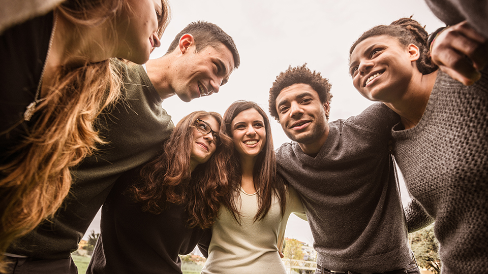 Junge Männer und Frauen stehen umarmend im Halbkreis. (Quelle: © iStock | franckreporter) Junge Männer und Frauen stehen umarmend im Halbkreis.