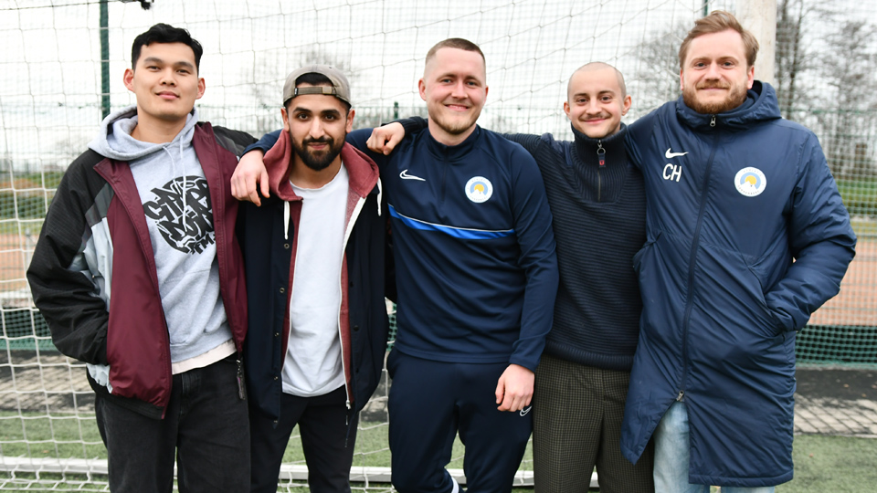 Fünf junge Männer porträtieren auf einem Sportplatz (Quelle: © BAMF | Kristin Kasten) Fünf junge Männer porträtieren auf einem Sportplatz