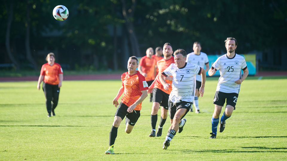 Fußballspieler zweier Teams rennen einem Fußballball hinterher. (Quelle: DOSB | Riedl) Fußballspieler zweier Teams rennen einem Fußballball hinterher.