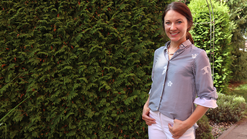 Eine Frau steht vor einer Hecke. (Quelle: BAMF) Eine Frau steht vor einer Hecke.