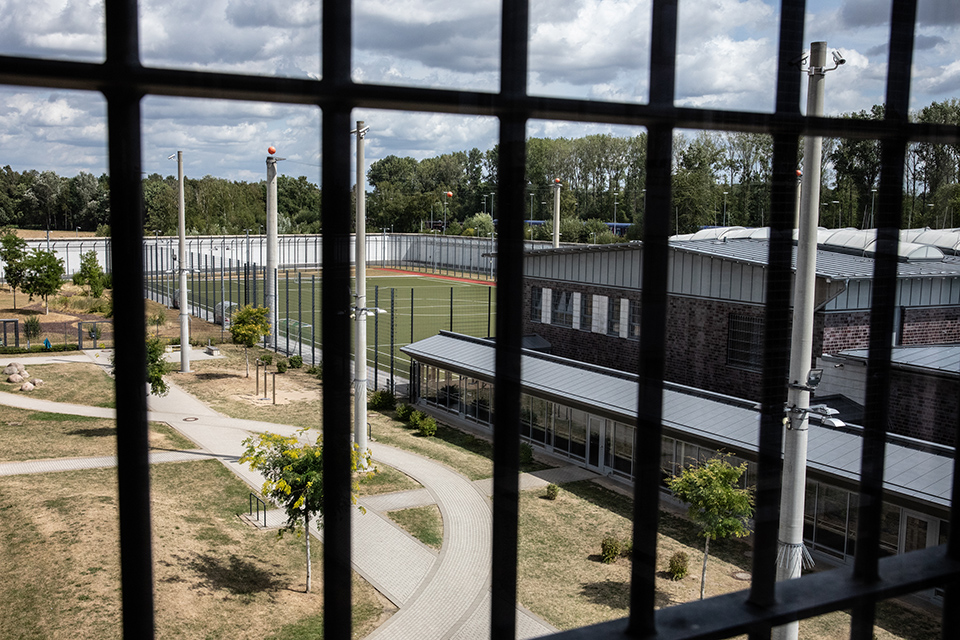 Gitterstäbe, dahinter ein Hof mit einem Gebäude und einem angrenzenden Sportplatz. (Quelle: Thomas Lobenwein) Gitterstäbe, dahinter ein Hof mit einem Gebäude und einem angrenzenden Sportplatz.