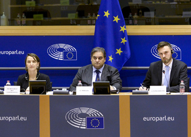 Eine Frau und zwei Männer sitzen auf dem Podium des EU-Parlaments