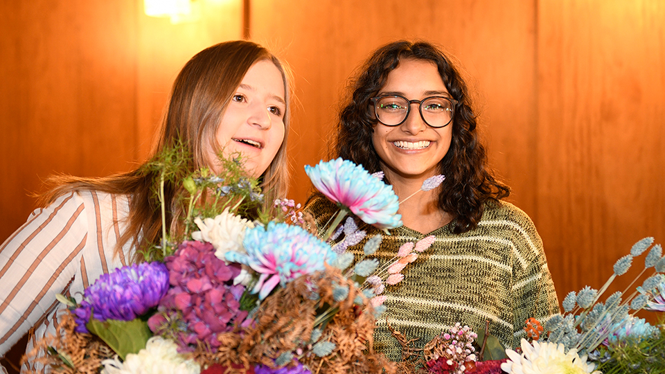 Zwei Frauen stehen nebeneinander und halten Blumensträuße in ihren Händen.