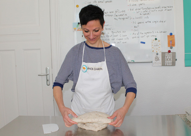 Eine Frau steht hinter einem Tisch und knetet Teig. (Quelle: BAMF | Gerd Fürstenberger) Eine Frau steht hinter einem Tisch und knetet Teig.