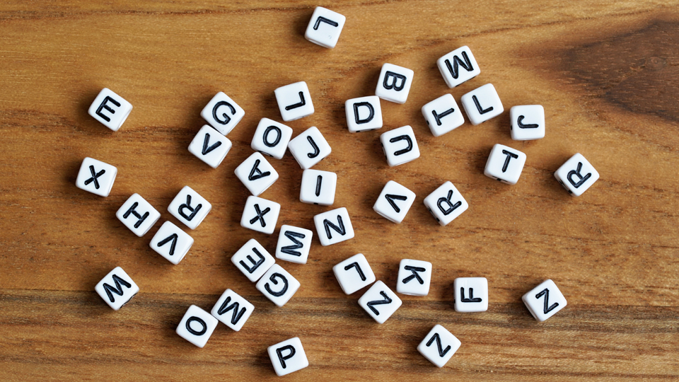 Viele kleine weiße Würfel mit unterschiedlichen Buchstaben liegen auf einem Holzuntergrund