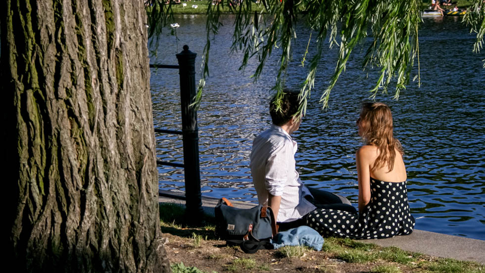Zwei Personen sitzen an einem Flussufer und unterhalten sich. (Quelle: ©GfHF_Picturing_Berlin_II | Ali Al Najjar) Zwei Personen sitzen an einem Flussufer und unterhalten sich.