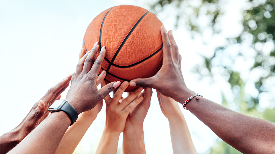 Viele Hände halten einen Basketball.
