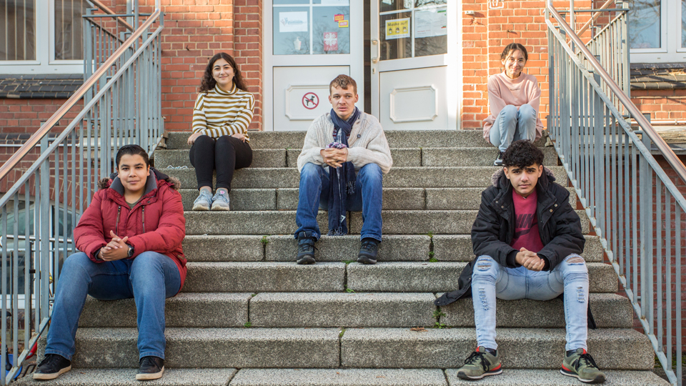 Fünf junge Menschen sitzen auf den Stufen einer Treppe.