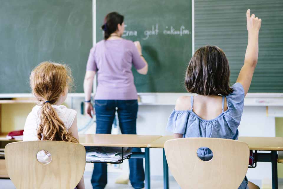 Zwei Kinder sitzen in einem Schulzimmer mit Blick auf die Tafel