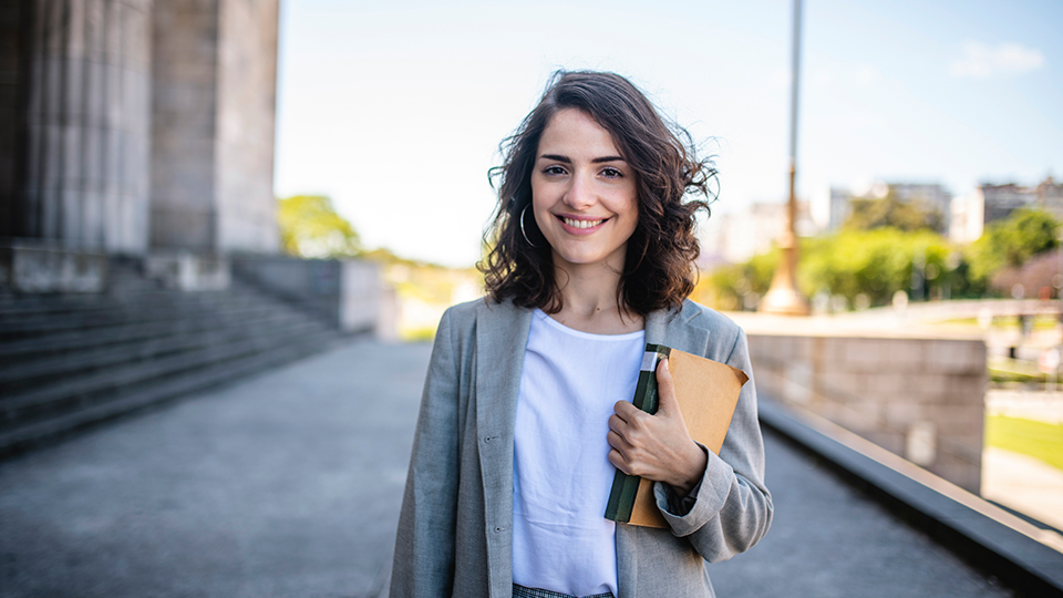 Eine junge Frau hält ein Buch in der Hand und lächelt. (Quelle: iStock | AzmanJaka) Eine junge Frau hält ein Buch in der Hand und lächelt.