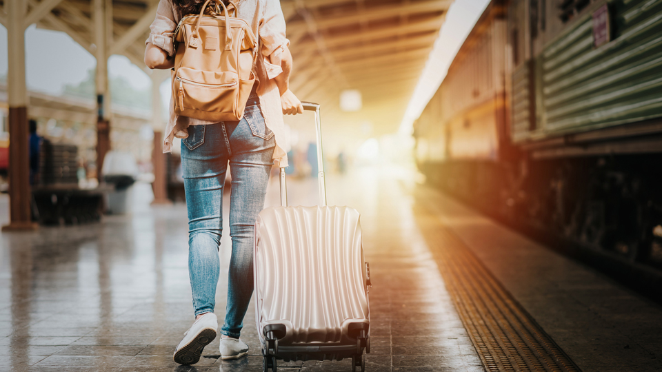 Eine Frau mit einem Rucksack und einem Koffer an einem Bahnsteig