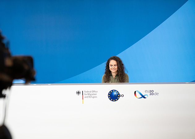 Eine Frau sitzt hinter einem Redepult (Source: BAMF) Eine Frau sitzt hinter einem Redepult